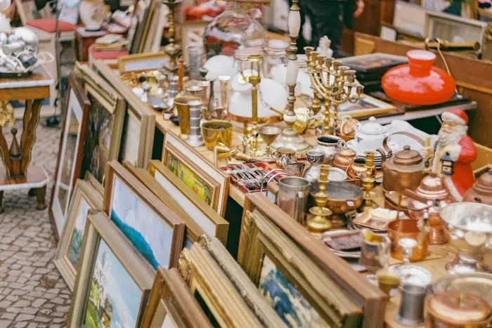 A flea-market table crowded with brass, glass and framed paintings